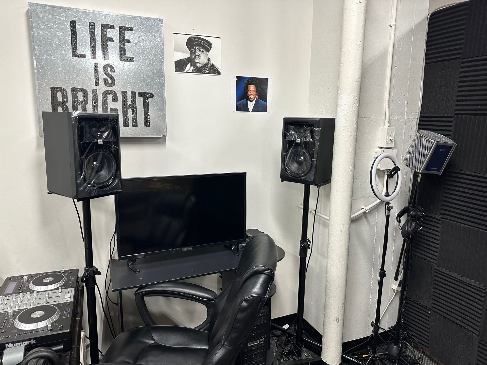 Recording studio setup: speakers, monitor, chair, artwork, soundproofing, and a microphone.