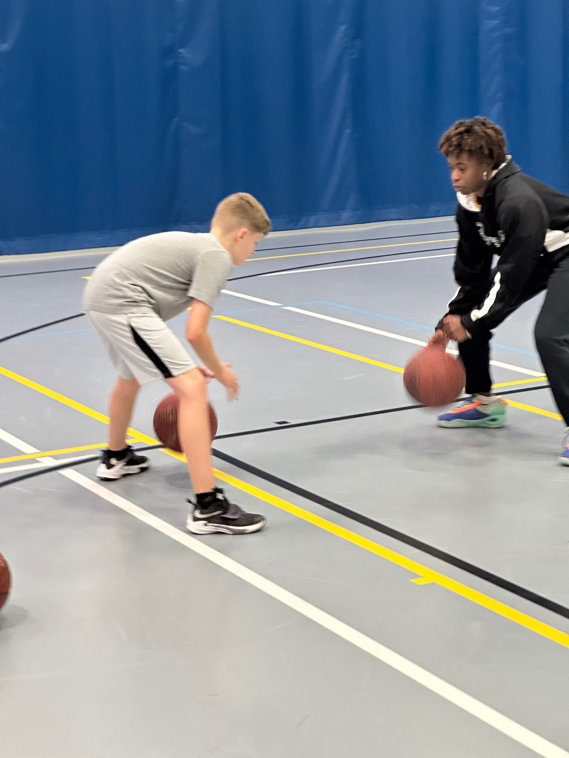 Boy dribbling basketball, practicing with a coach indoors. Gym floor with blue walls.