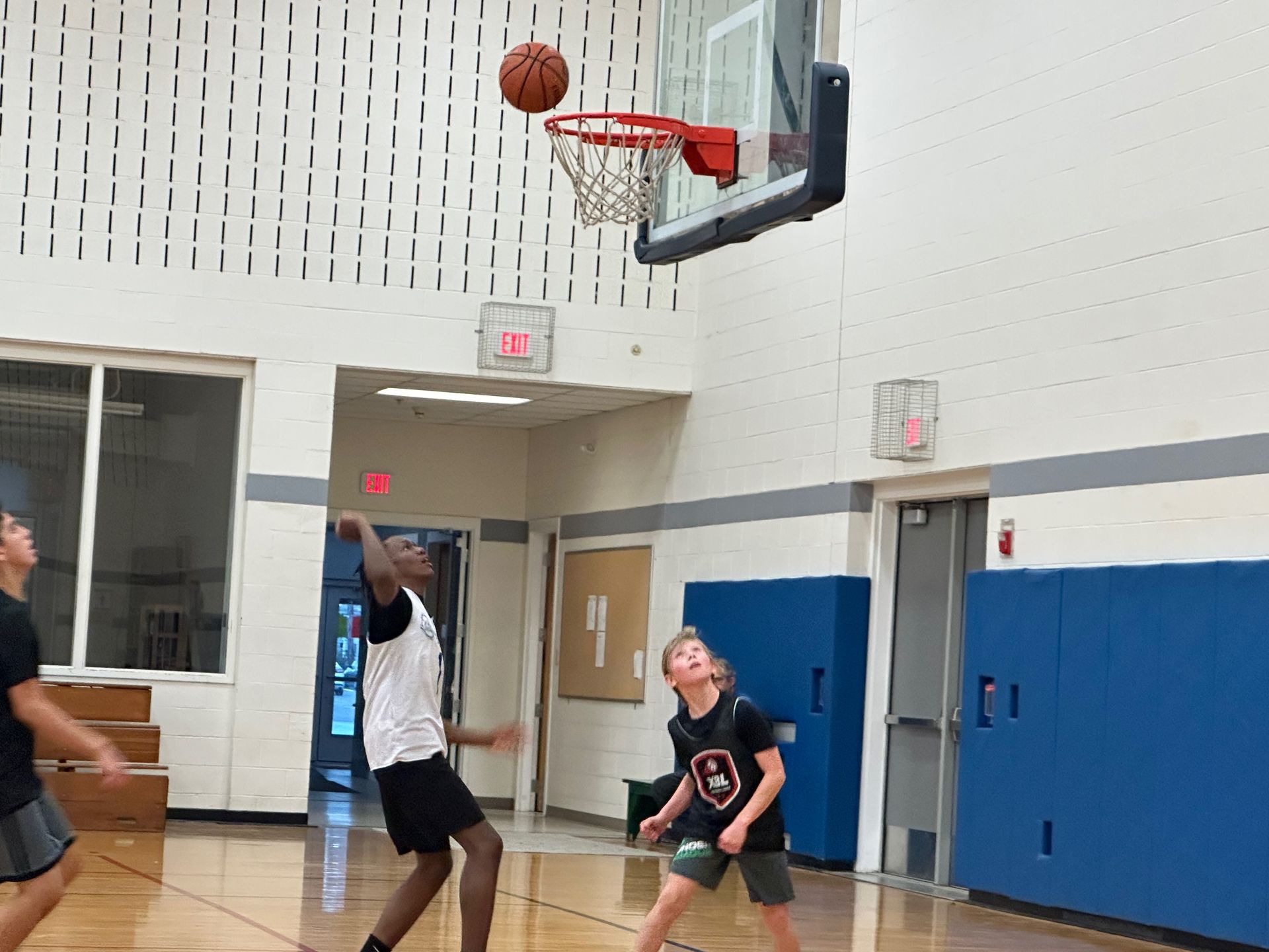 Basketball ball going through hoop during a game. Players watch in indoor gym.