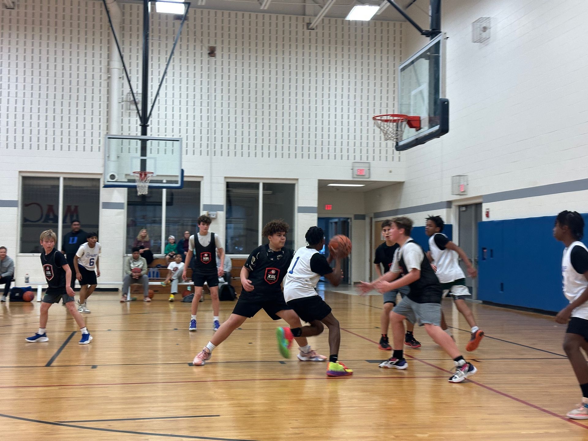 Basketball game in a gym. Players in jerseys dribble, defend, and shoot near the hoops.