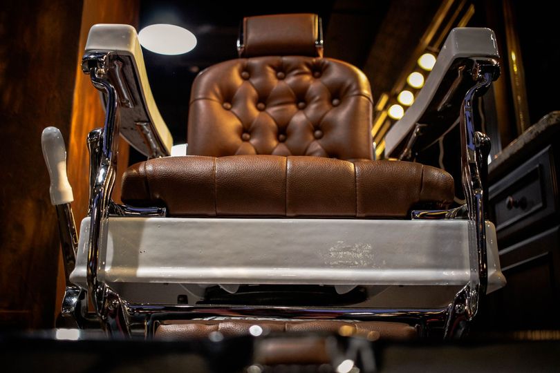 A brown tufted leather barber chair with chrome accents in a dimly lit salon.