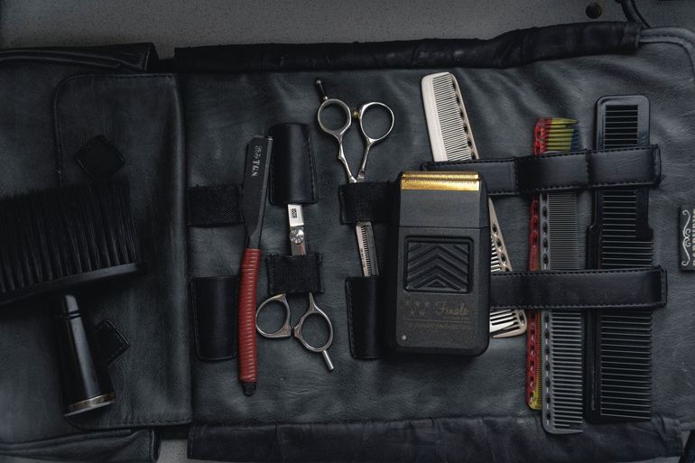 A black leather roll-up kit containing barber tools: scissors, a straight razor, a shaver, and several combs.