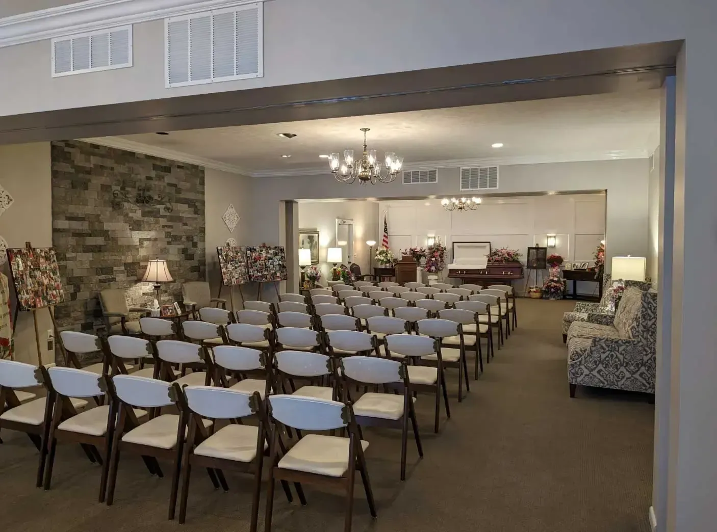 Rows of white chairs set up in a hall for an indoor event, with floral arrangements and chandeliers.