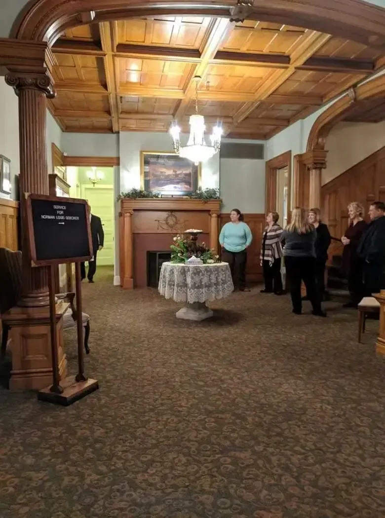 Elegant banquet room with ornate wood ceiling, fireplace, round table, and several people standing near the wall