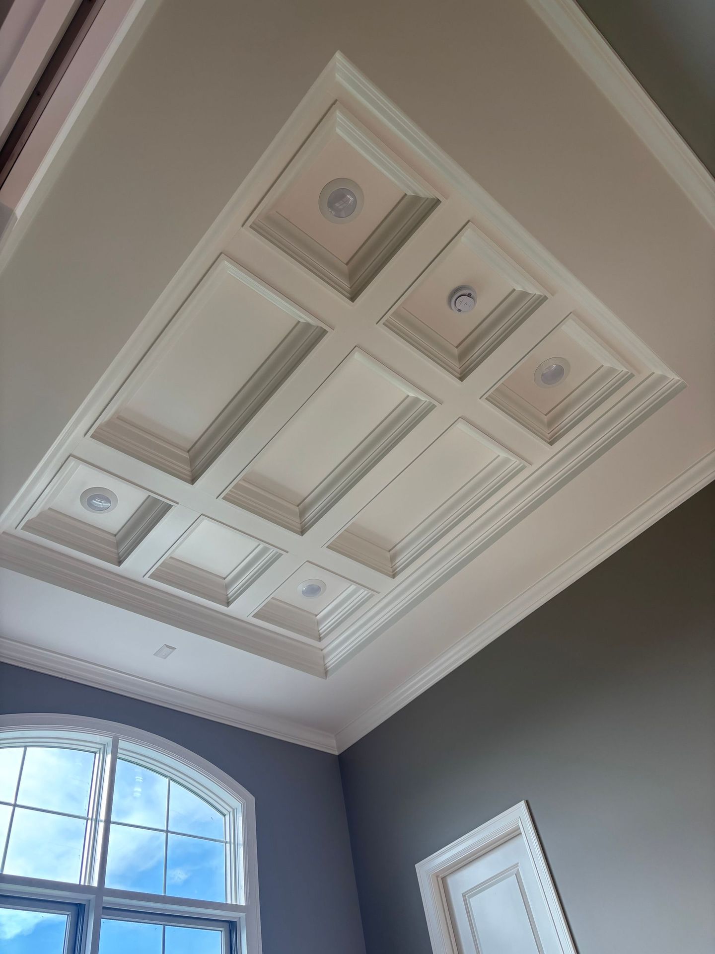 White coffered ceiling with recessed lighting, decorative molding, and a window with a blue sky view.
