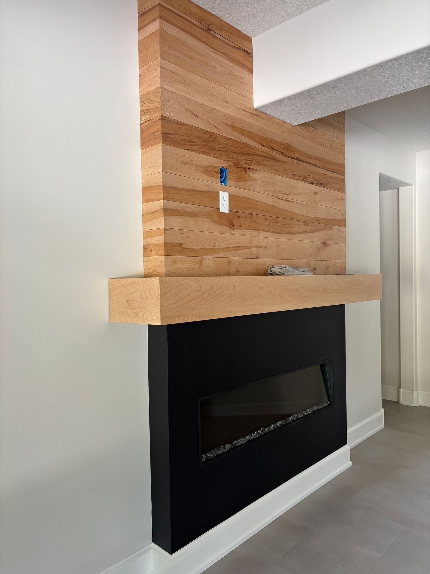 Modern fireplace with black surround, wood accent wall and mantle.