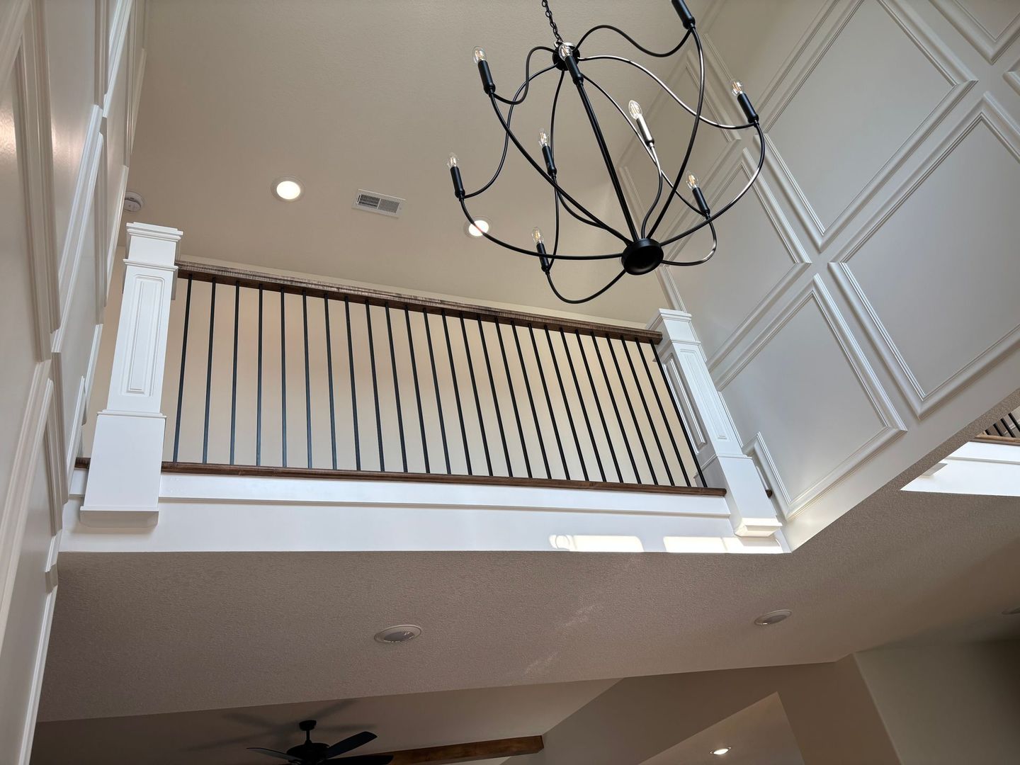 View from below of a balcony railing with a chandelier hanging from the high ceiling.