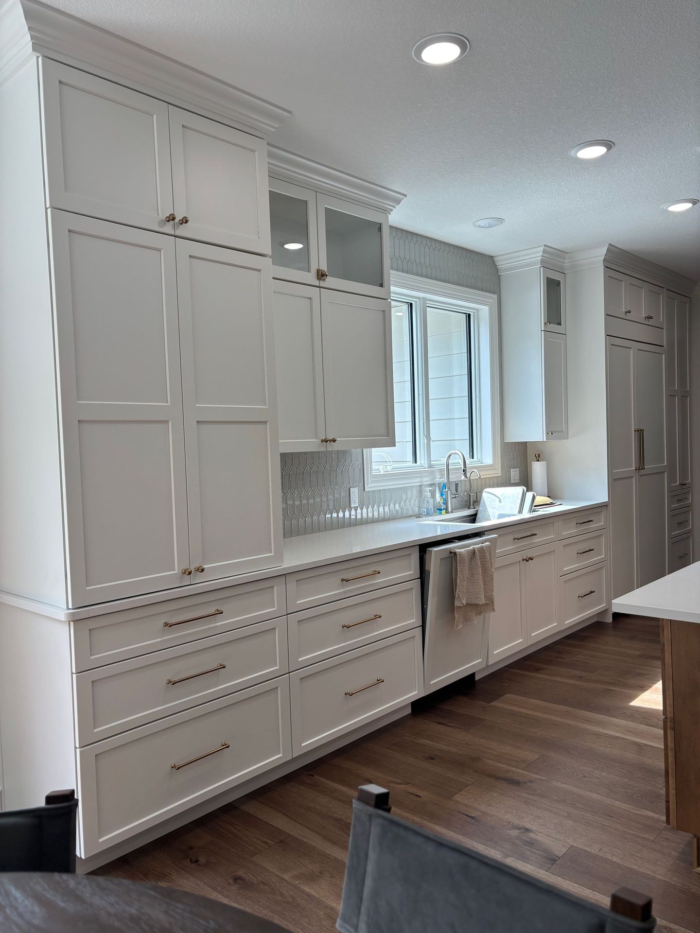 White kitchen cabinets with drawers and upper cabinets by a window with a neutral backsplash.