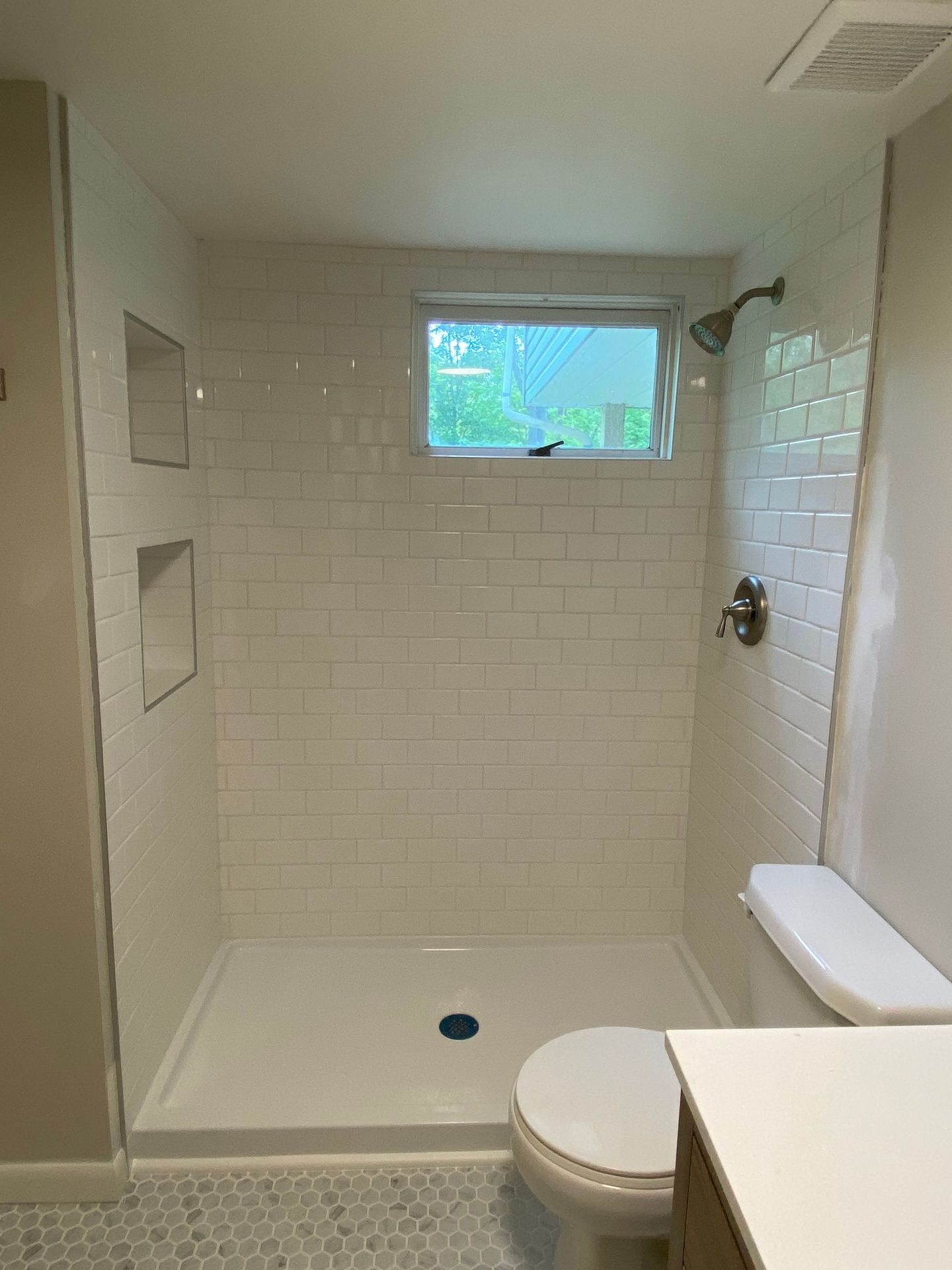 Bathroom with white subway tile shower, toilet, and window.