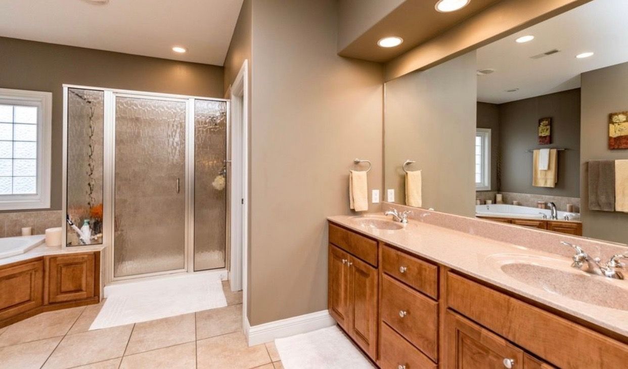 Spacious bathroom with brown cabinets, double sinks, shower, and bathtub; neutral color palette.