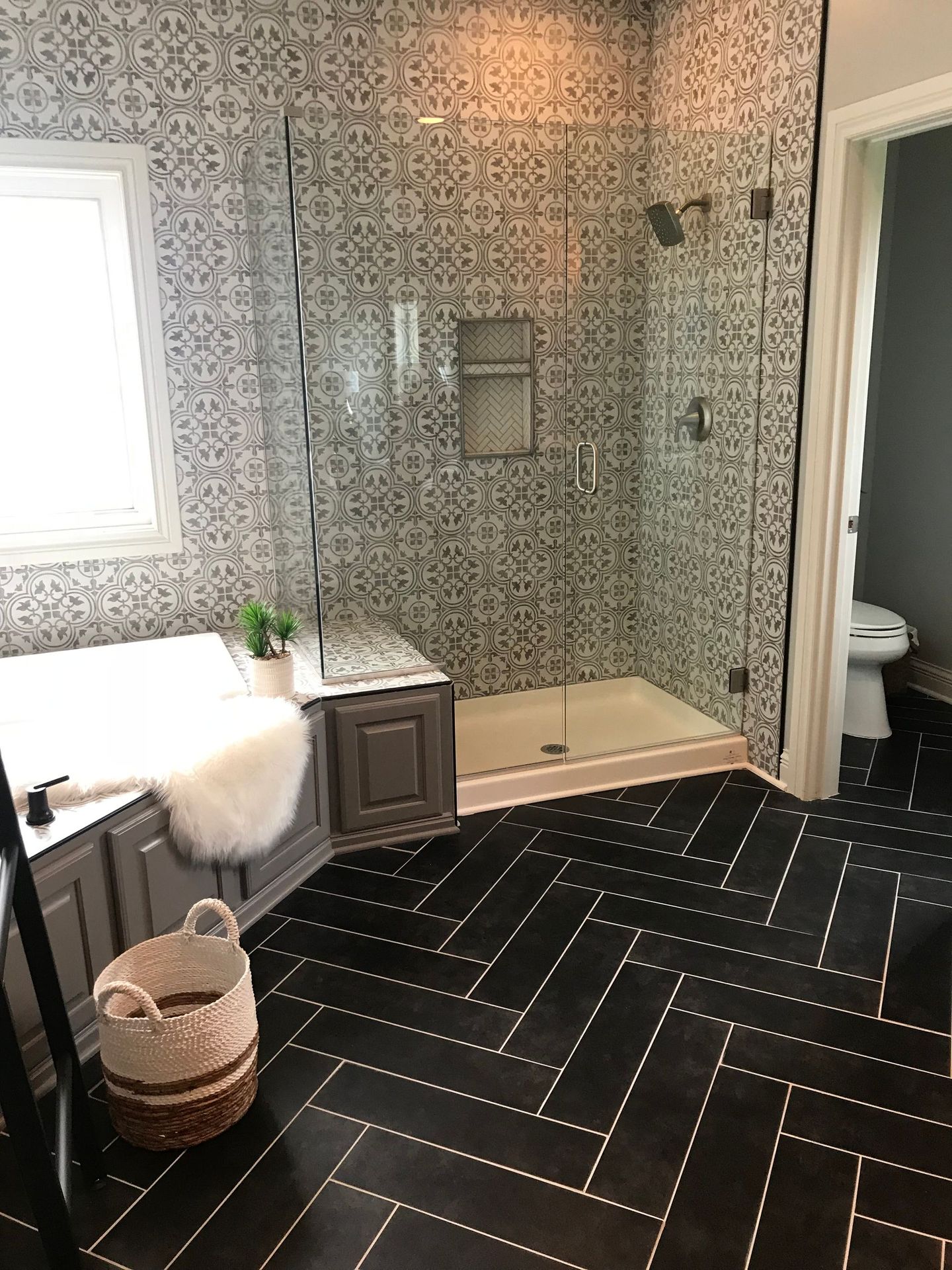 Bathroom with black herringbone tile floor, gray tile walls, glass shower, and a tub.