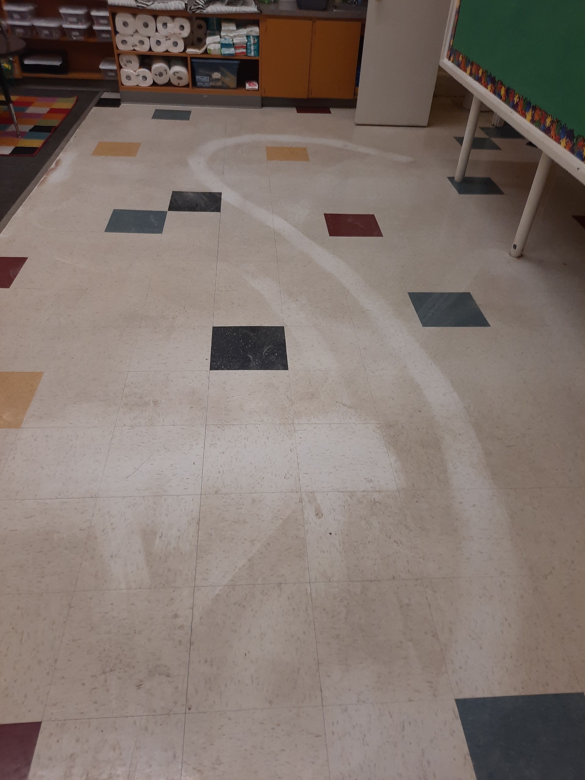 A dirty tiled floor in a classroom with a green board in the background