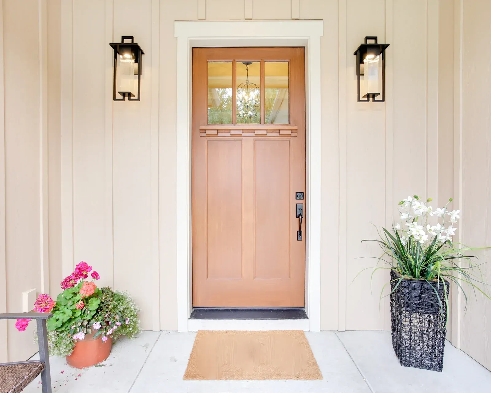 The front door of a house with a door mat and flowers on the porch.