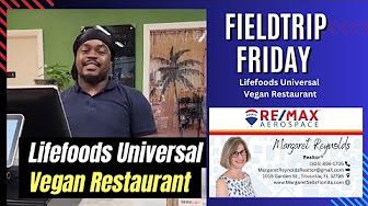 A man is standing in front of a laptop and a business card for a vegan restaurant.