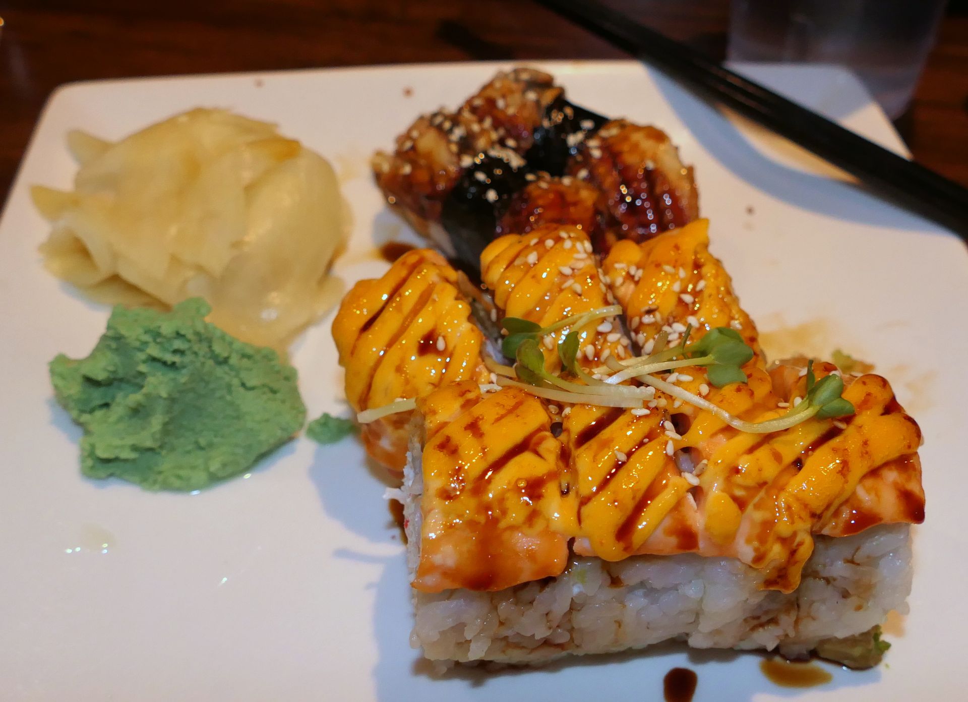 Plated sushi with sauce drizzle, wasabi, and pickled ginger on a white dish