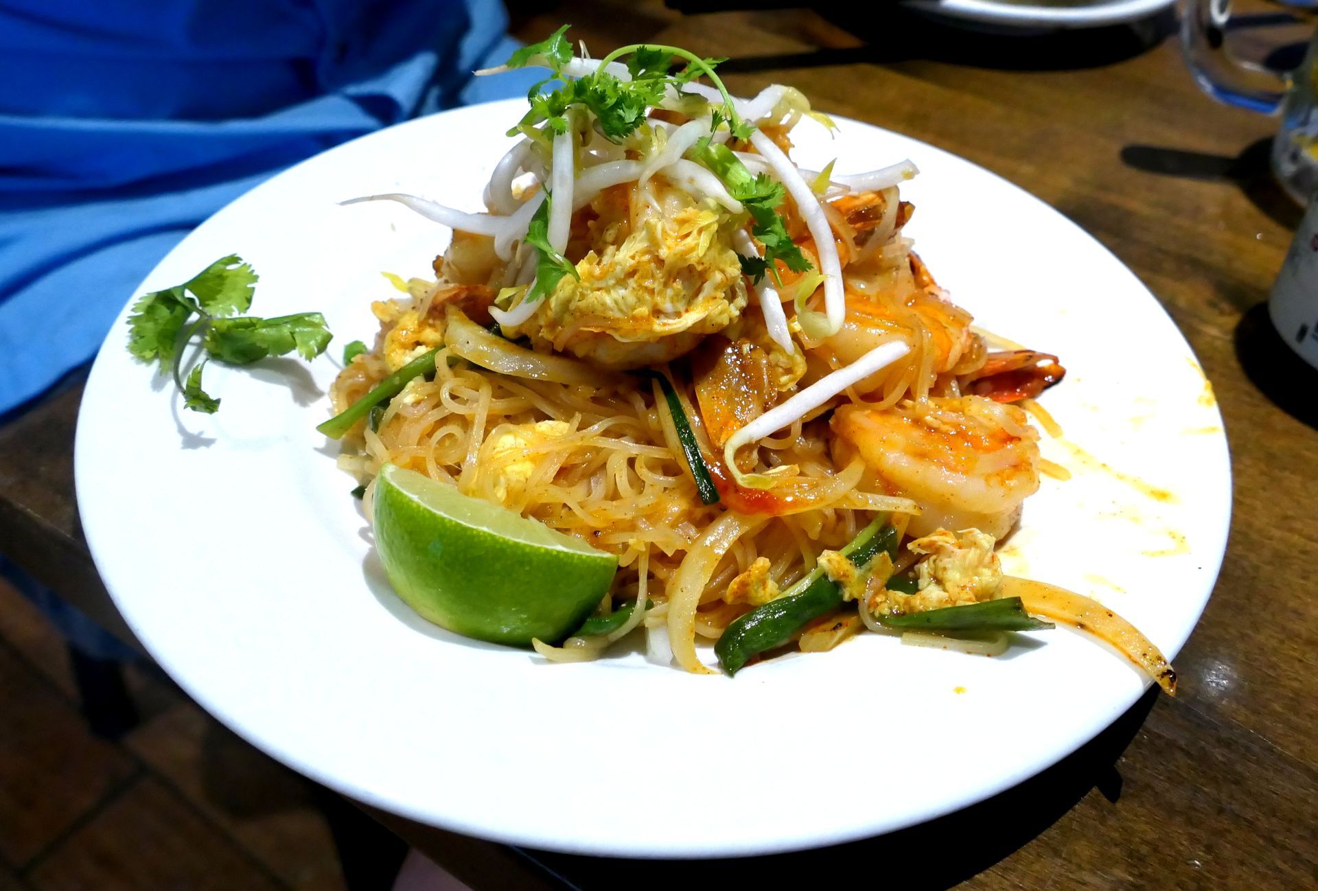 Plate of shrimp noodle dish garnished with bean sprouts and lime wedge on a table