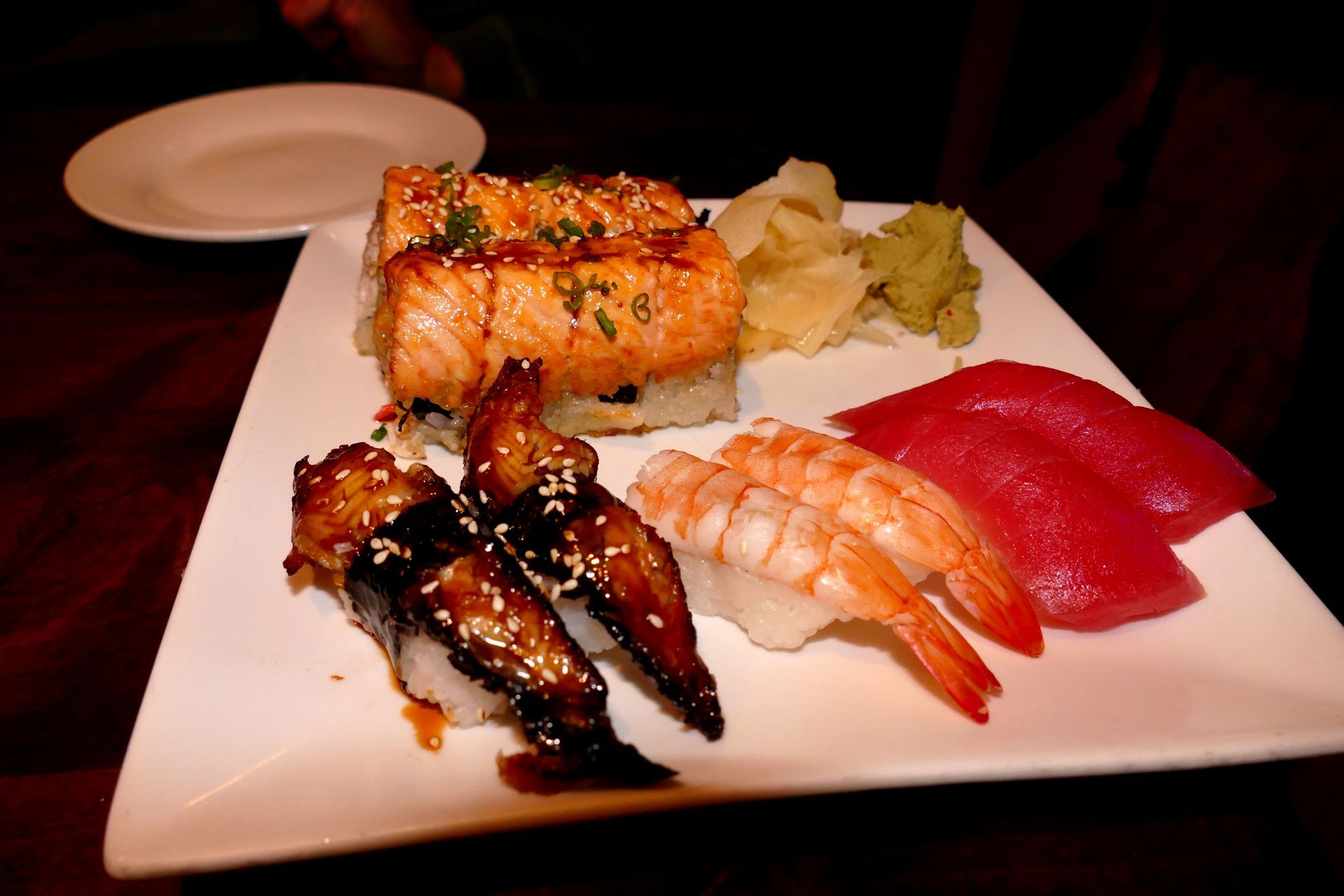 Assorted sushi platter on a white plate with salmon, tuna, eel, and ginger