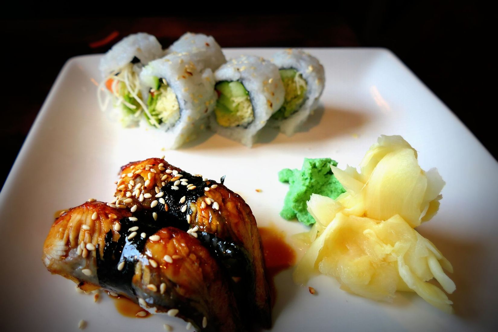 Sushi rolls and glazed chicken on a white plate with pickled ginger and broccoli.