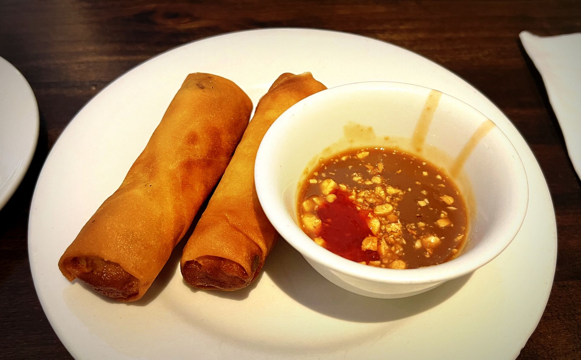 Two fried spring rolls on a white plate with a bowl of dipping sauce