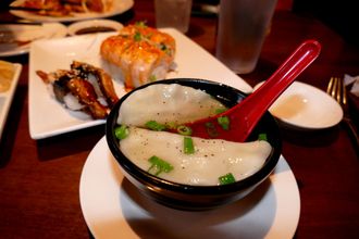 Bowls of Asian dishes on a restaurant table, including soup with a red spoon and sushi on white plates