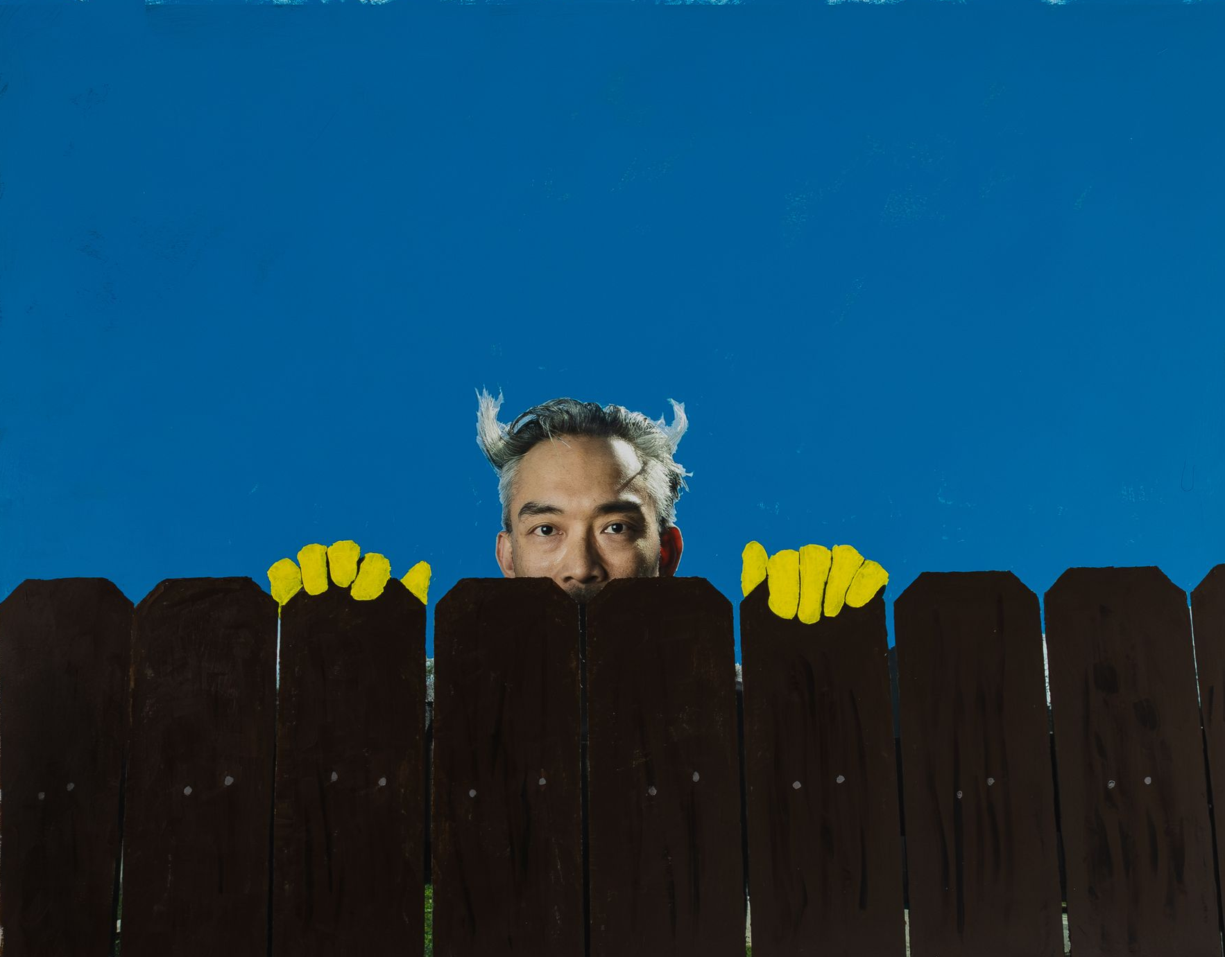man peering over black fence with devil horns and yellow gloves