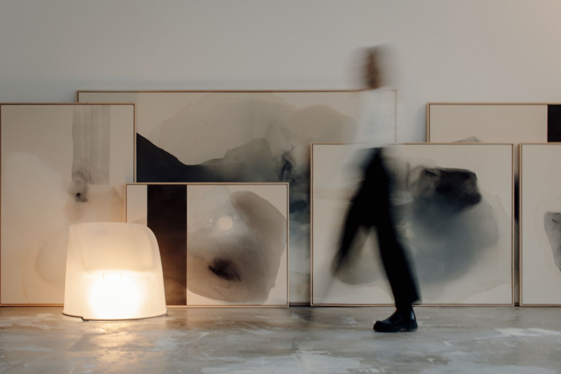 Joy Kinna walking past her large paintings, blurred with movement. in the corner of the shot there is an opaque white chair that has a light inside, giving it the appearance of it glowing. shot by Brit Gill Photography