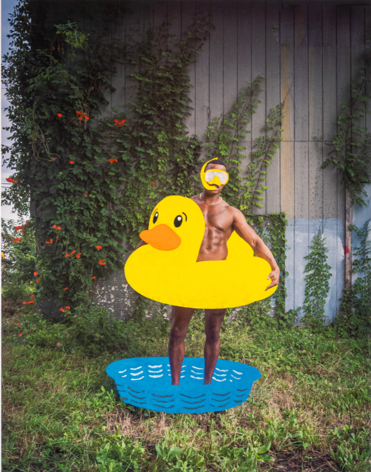 photograph of a man standing in a kiddie pool holding a yellow duck floatie and wearing yellow goggles