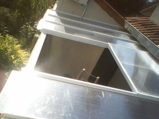 Marco de ventana blanco inclinado junto a un tejado, con la luz del sol reflejándose en el cristal.