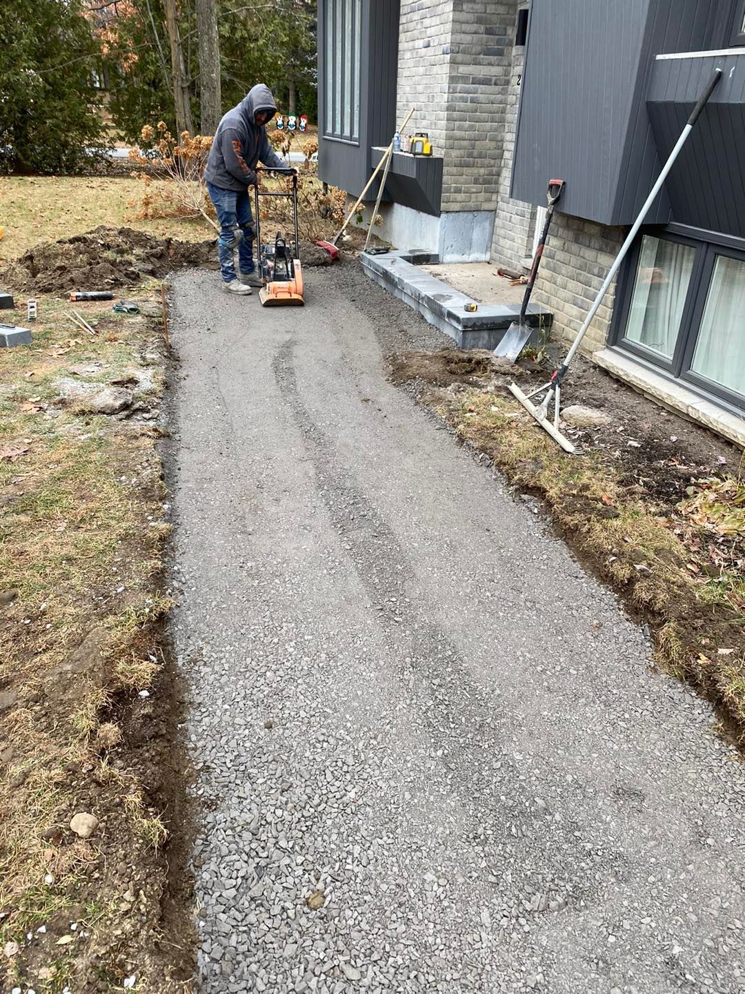 Une personne compacte un chemin de gravier avec une machine à côté d'une maison.