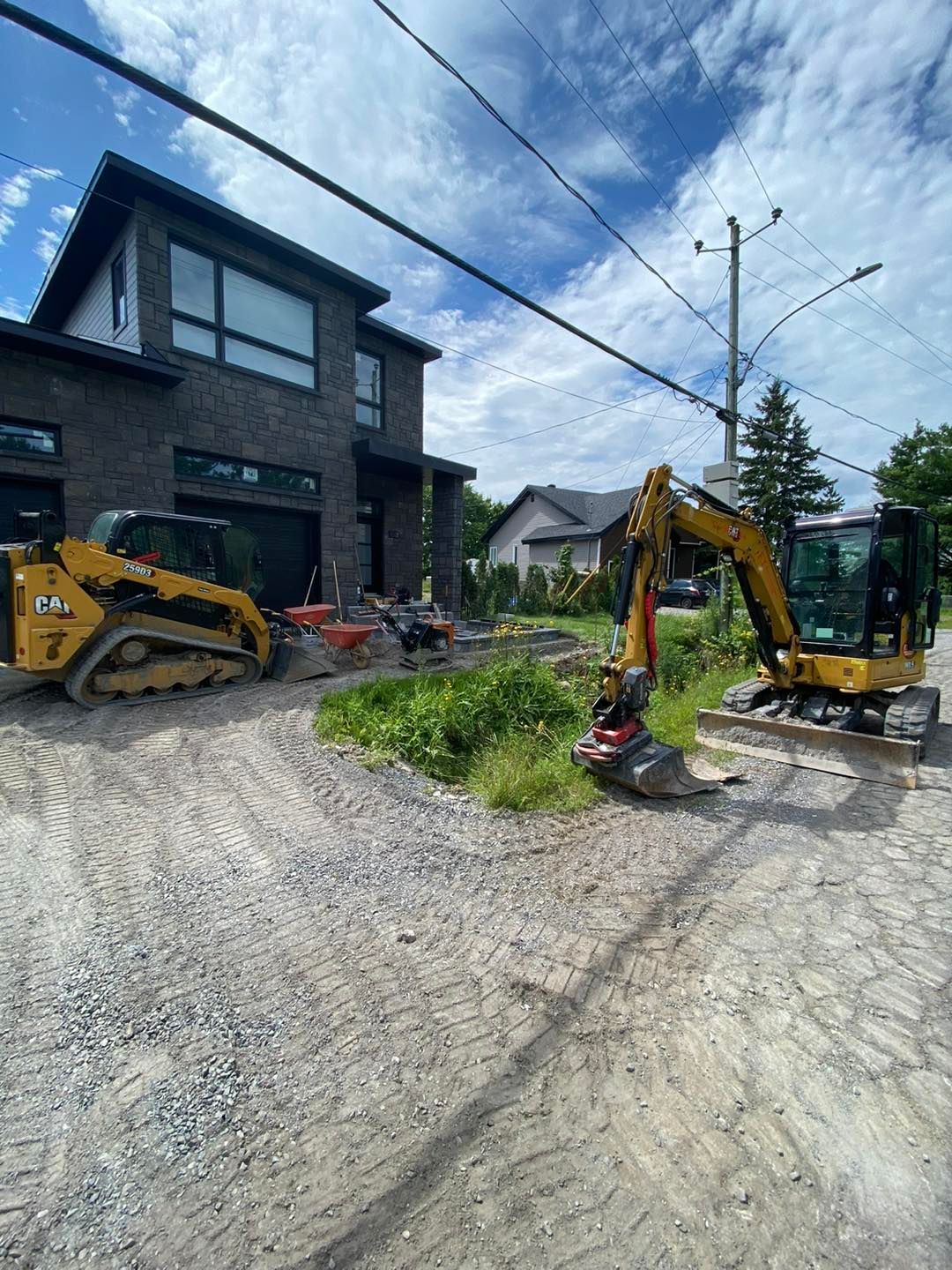 Chantier de construction avec deux engins jaunes devant une maison moderne en briques.