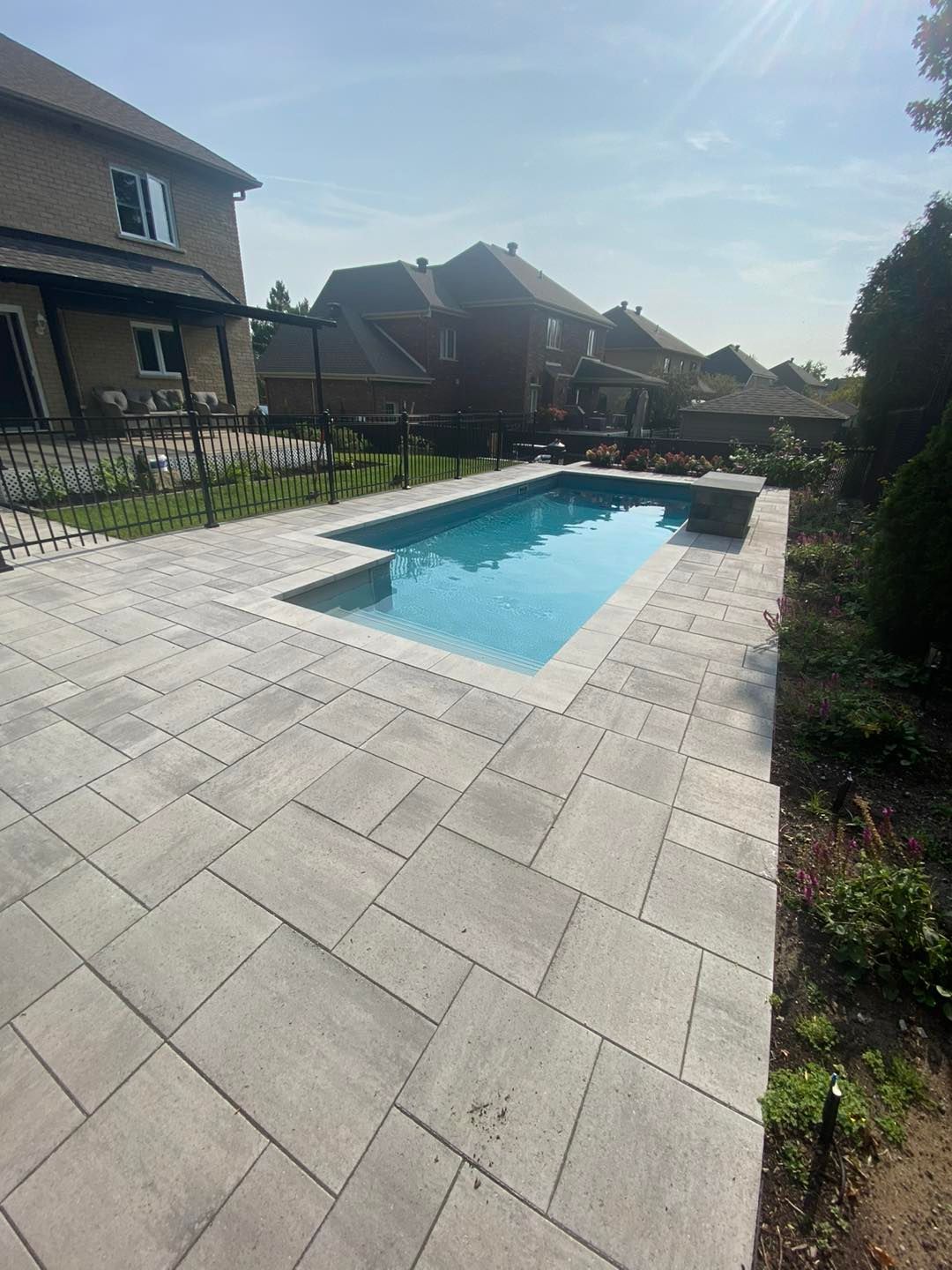 Piscine rectangulaire entourée de pavés gris clair dans un jardin.