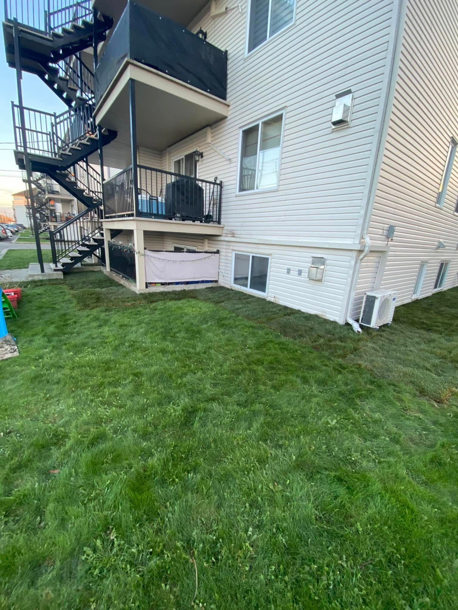 Extérieur du bâtiment avec de l'herbe au premier plan. Escalier et balcon noirs à gauche. Bardage blanc.