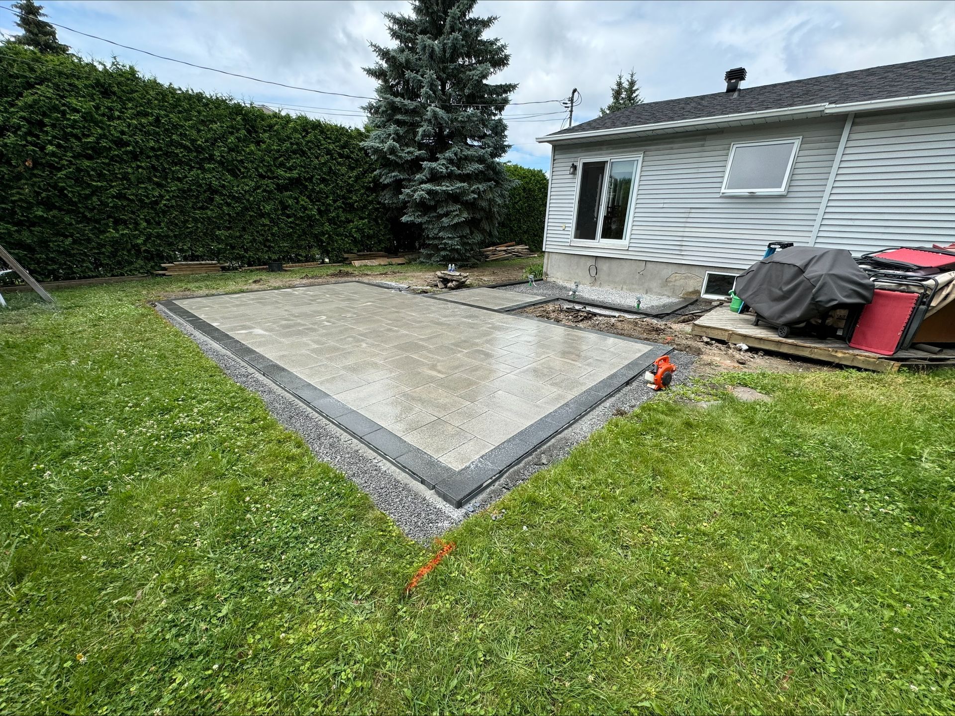 Une terrasse en béton coulé dans un jardin, à côté d'une maison et d'une pelouse verdoyante.