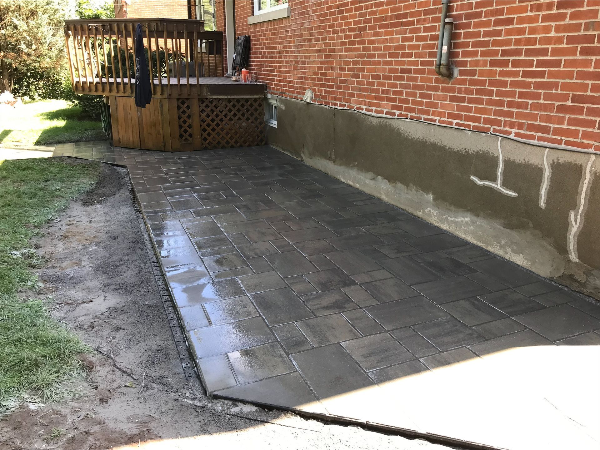 Terrasse nouvellement pavée de briques gris foncé, jouxtant une maison en briques rouges et une terrasse en bois.