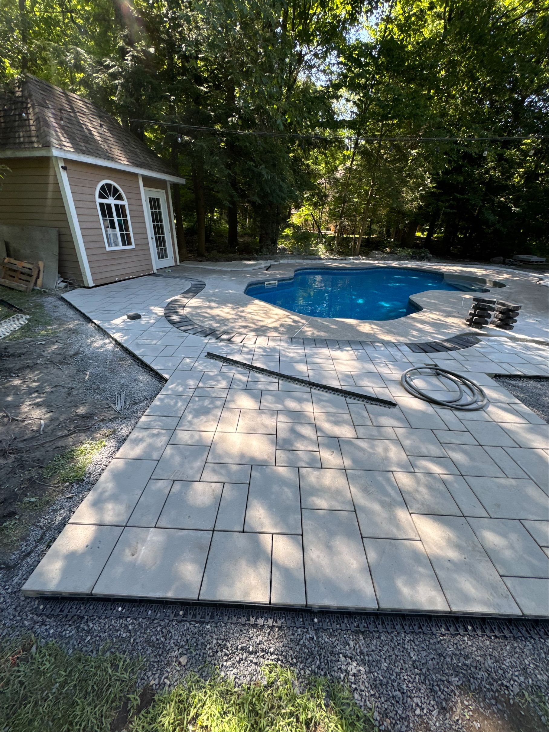 Pose de dalles de terrasse autour d'une piscine. Un petit bâtiment est visible en arrière-plan.