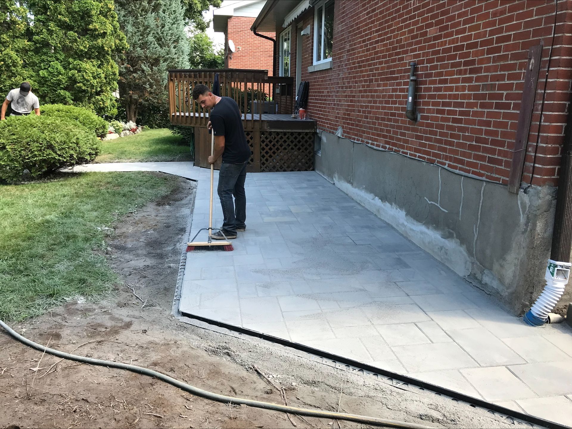 Un homme balaie des dalles de terrasse neuves à côté d'un bâtiment en briques. Une autre personne est visible en arrière-plan.