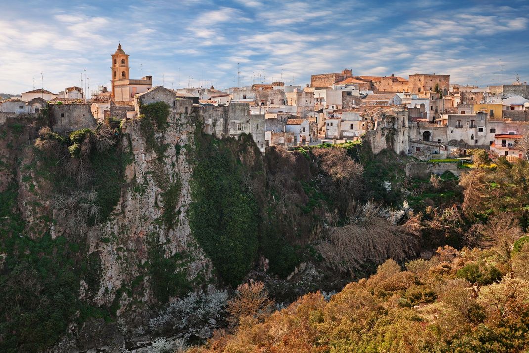 Villaggio a picco sulla scogliera con edifici in pietra e una chiesa sopra una ripida gola verde al tramonto