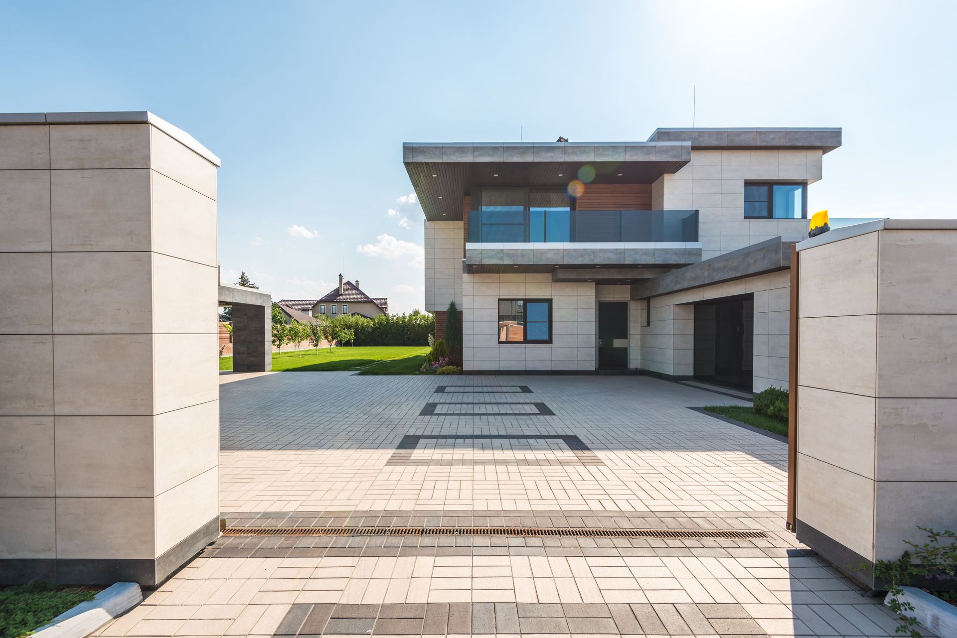 Casa moderna a due piani con vialetto pavimentato e cancello aperto sotto un cielo azzurro limpido