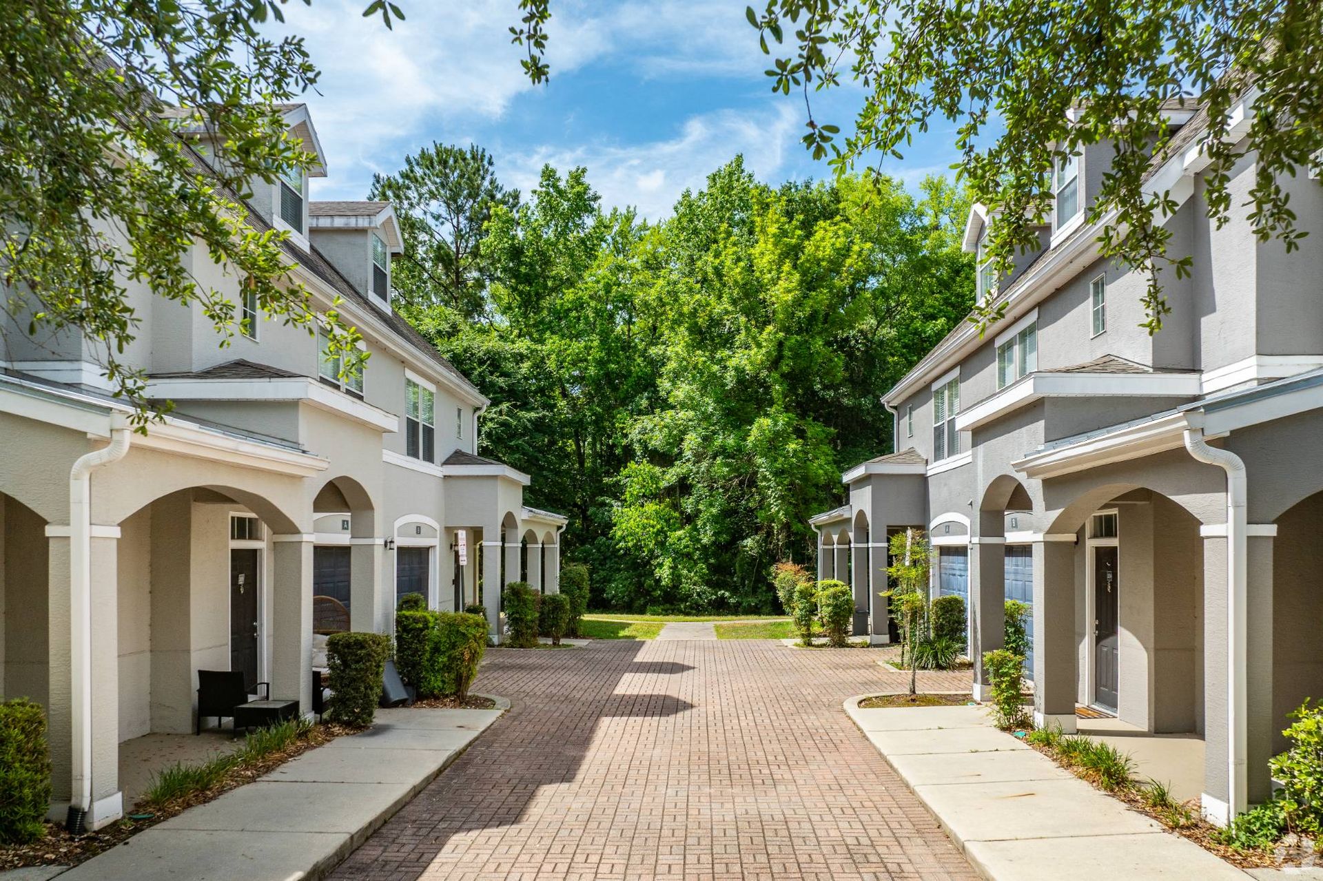 Exterior view of townhouse-style apartment buildings lining a brick courtyard with trees at Uptown Village Apartments in Gainesville, FL.