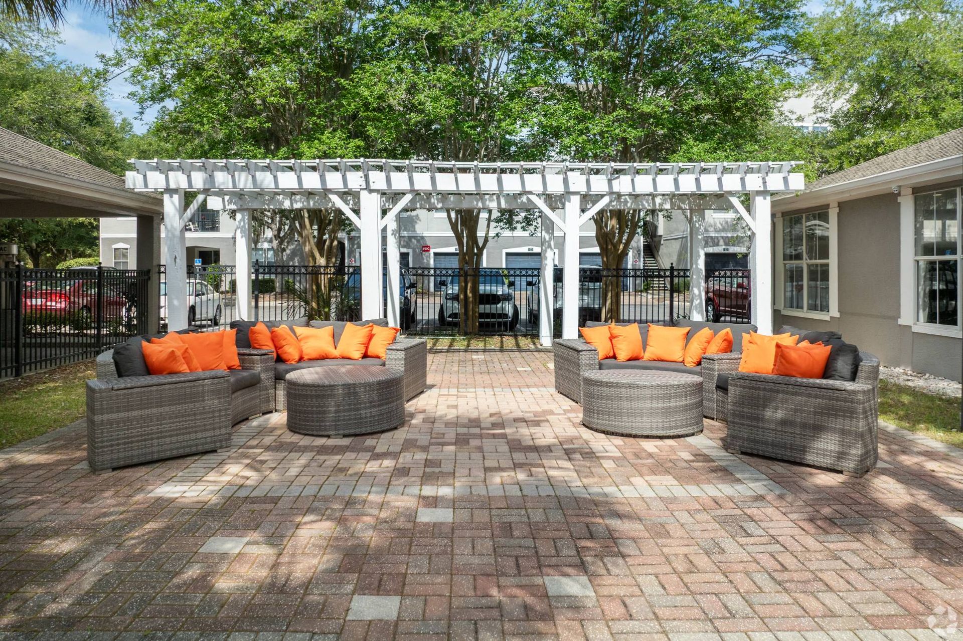 Outdoor community lounge with wicker seating and orange cushions under a white pergola at Uptown Village Apartments in Gainesville, FL.