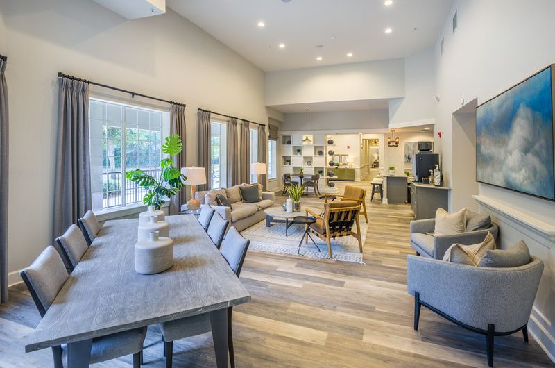 Residential community lounge with sofa seating, a large dining table, and a kitchenette at Uptown Village Apartments in Gainesville, FL.
