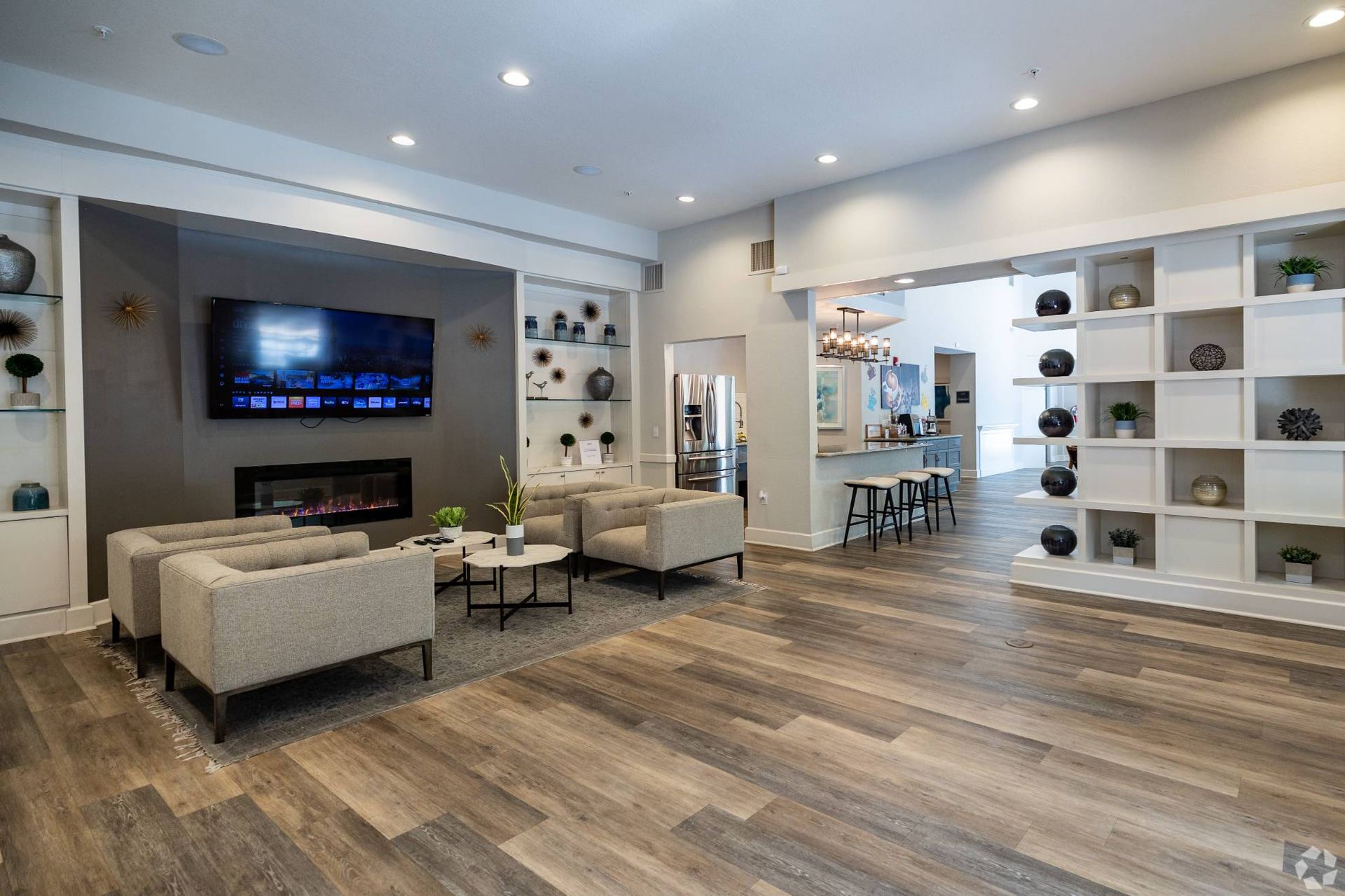 Modern resident lounge with couches, a wall-mounted TV, fireplace, and open kitchen at Uptown Village Apartments in Gainesville, FL.