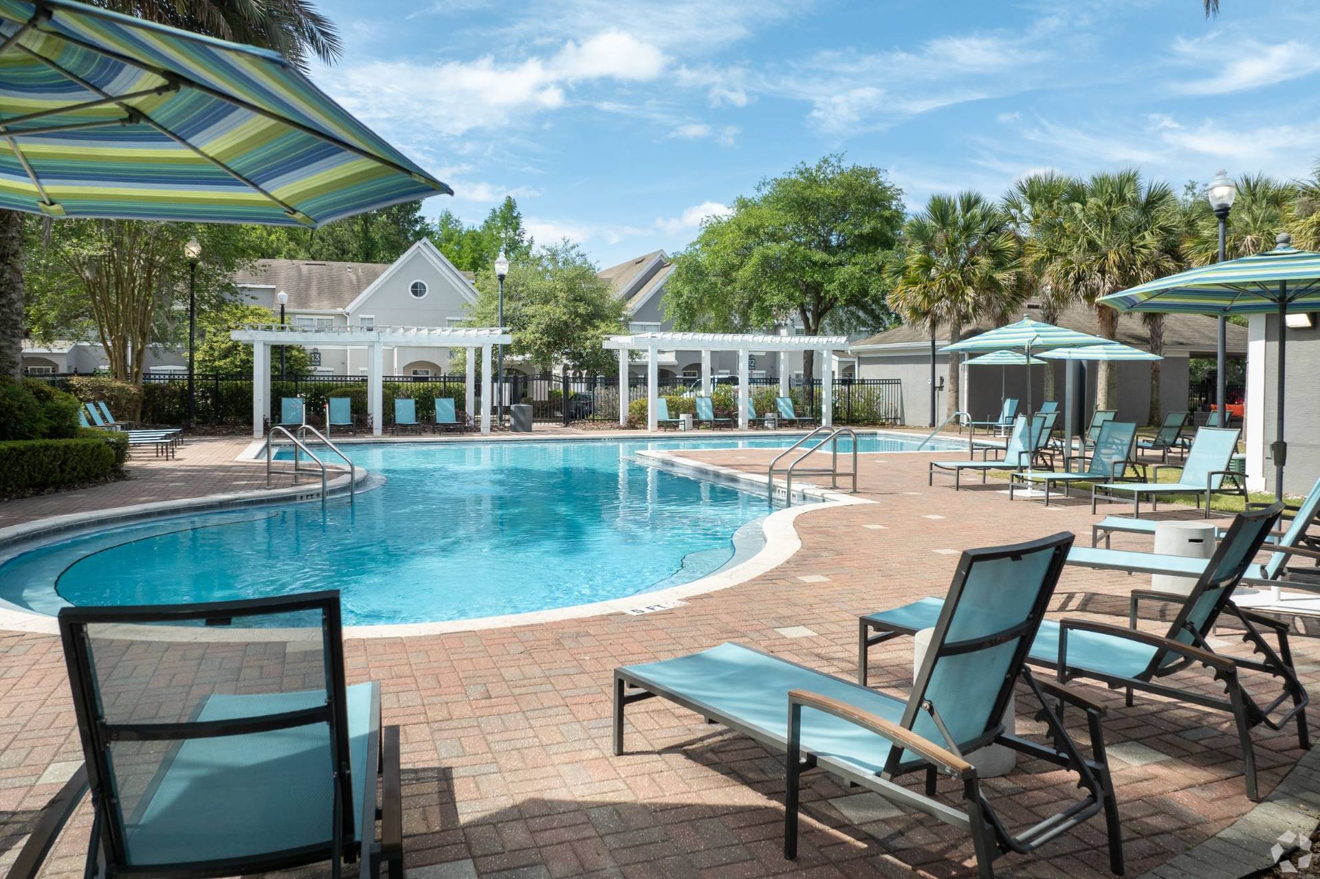 Outdoor apartment community pool with lounge chairs and striped umbrellas at Uptown Village Apartments in Gainesville, FL.