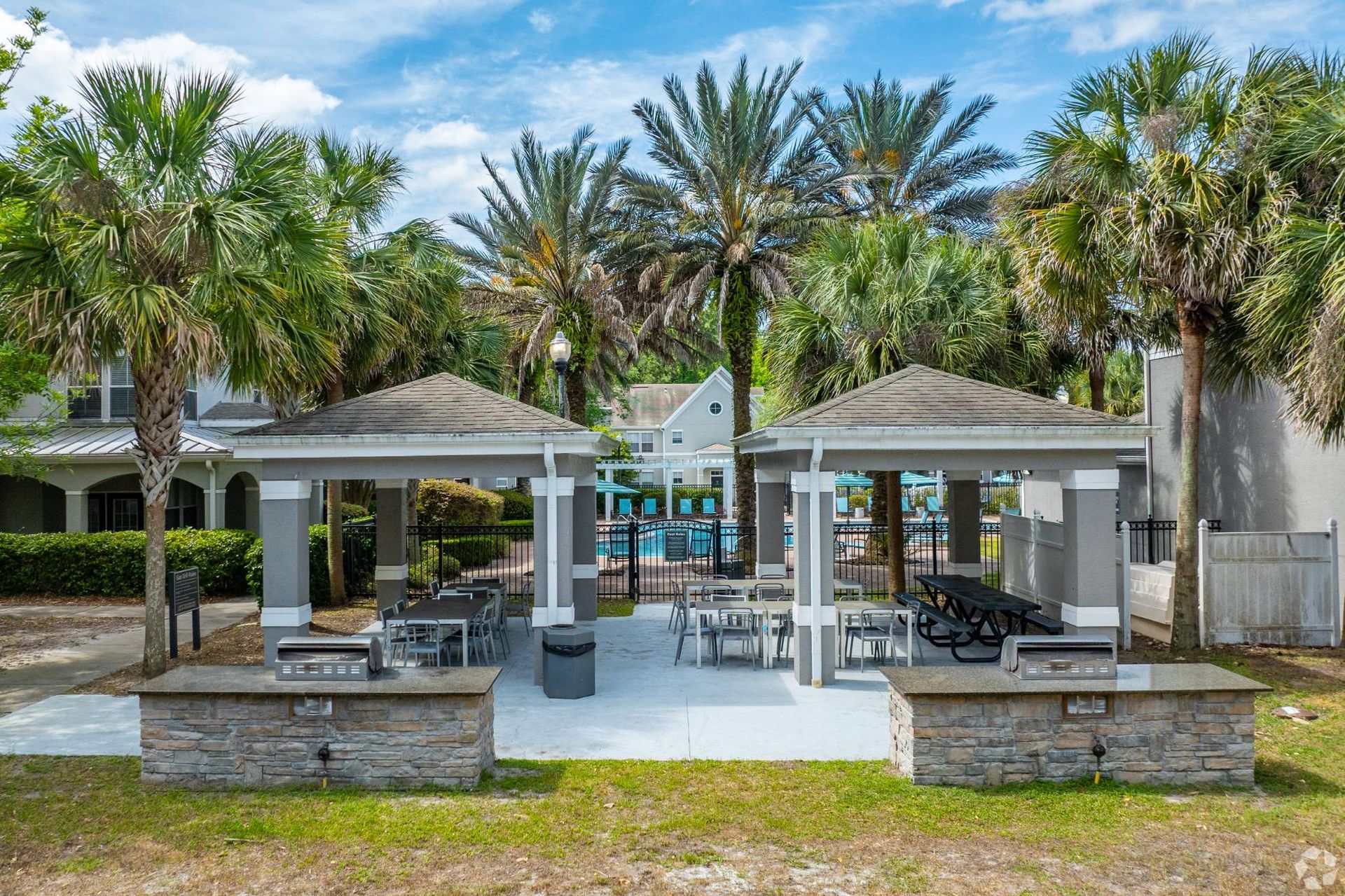 Outdoor community pool area with palm trees, shaded pavilions, and seating at Uptown Village Apartments in Gainesville, FL.