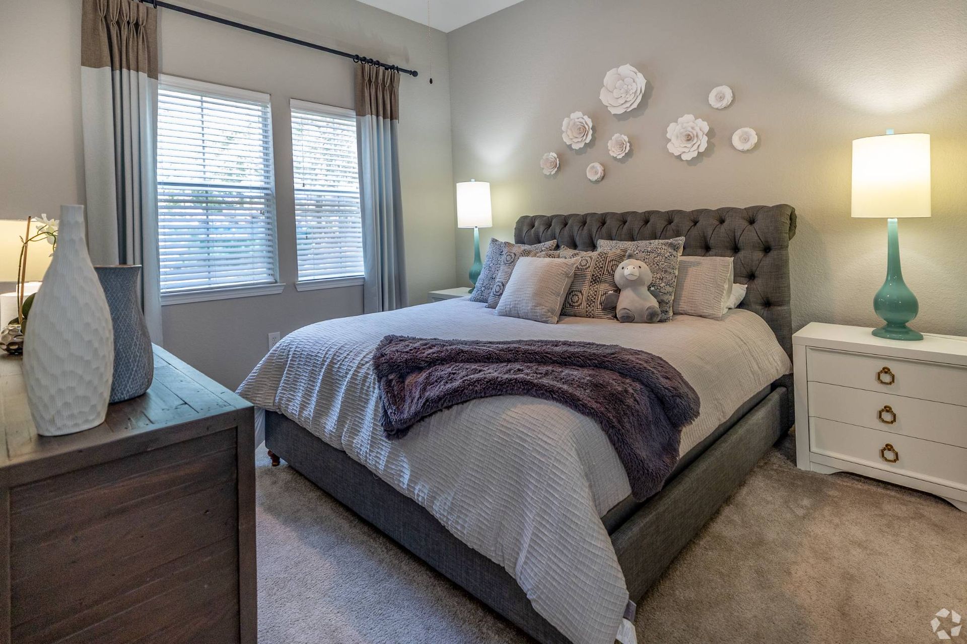 Bedroom in apartment with tufted headboard, two nightstands, lamps, and wall decor at Uptown Village Apartments in Gainesville, FL.