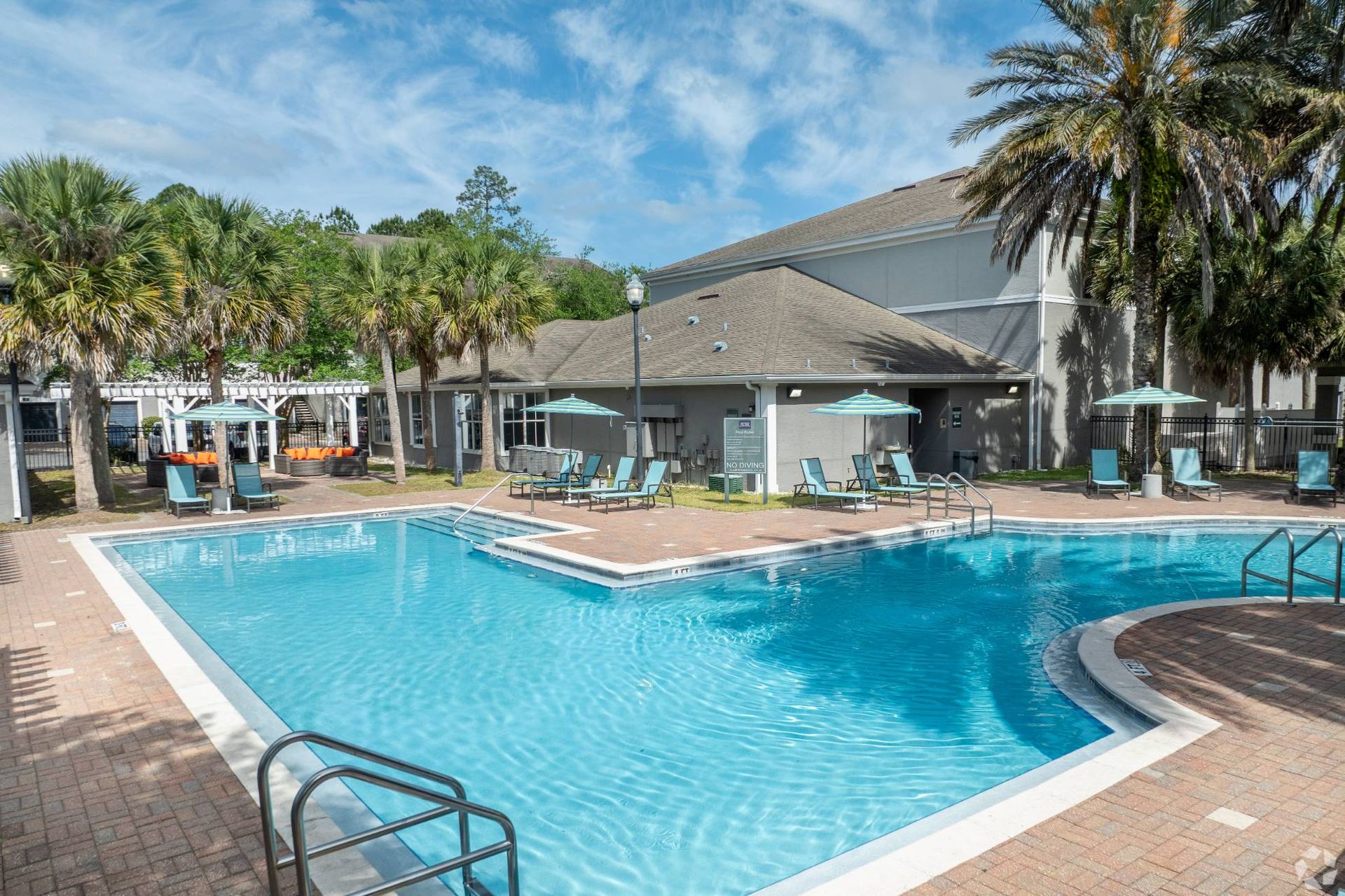 Outdoor apartment community pool with lounge chairs, umbrellas, and palm trees at Uptown Village Apartments in Gainesville, FL.