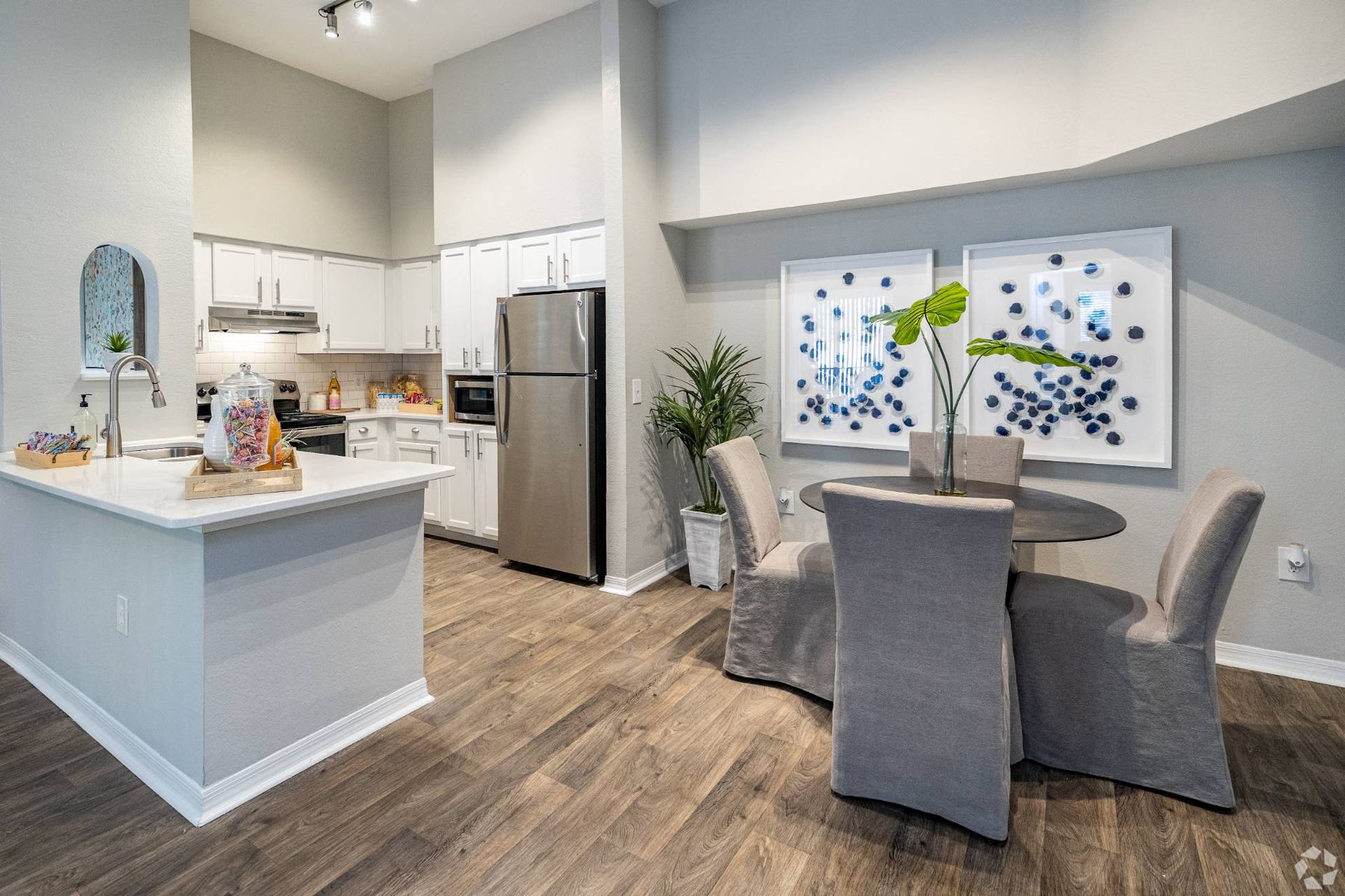 Open-concept kitchen and dining area with white cabinets, stainless appliances, and two framed blue abstract art pieces at Uptown Village Apartments in Gainesville, FL.