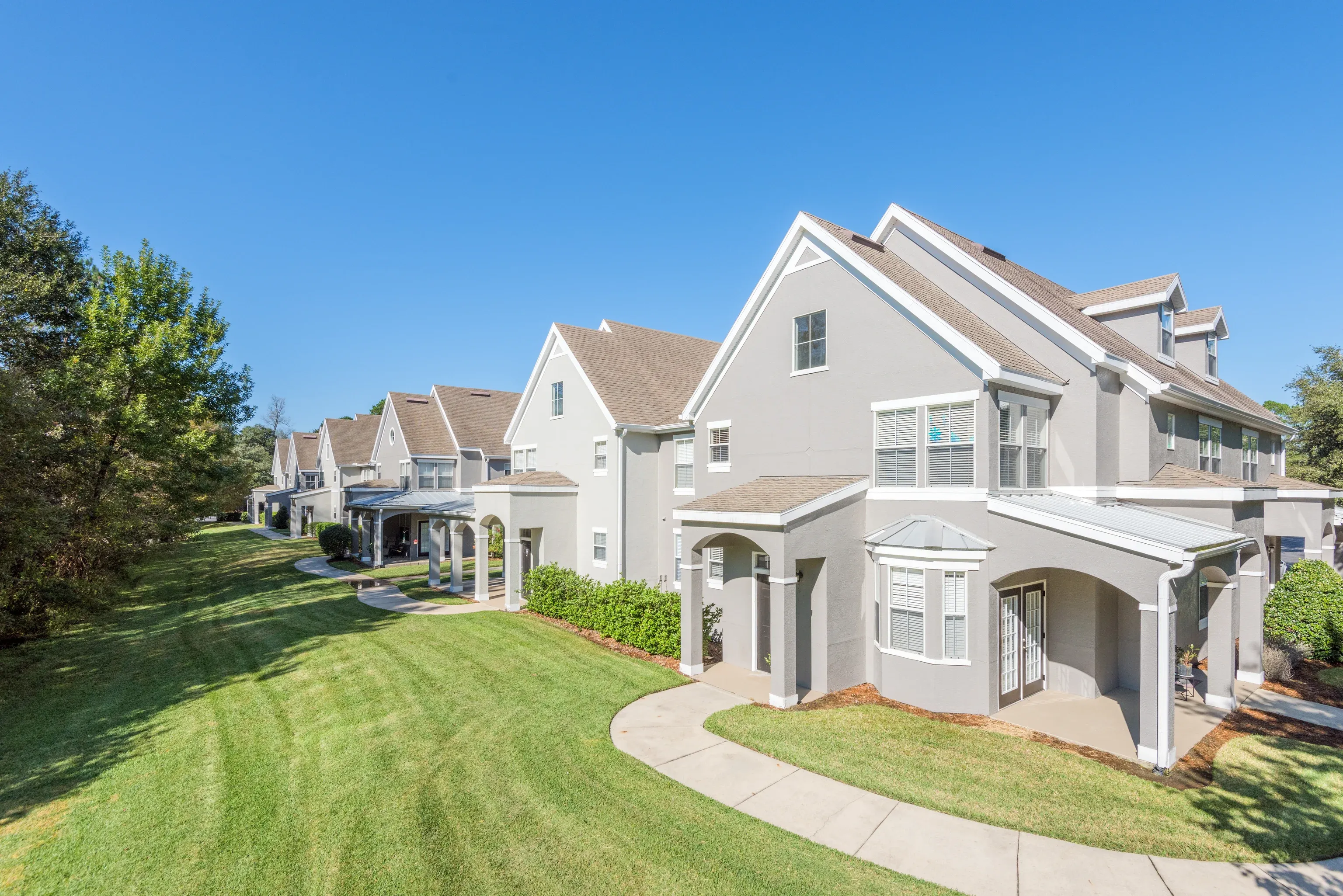 Row of townhome-style apartment buildings along a curved walkway with a green lawn at Uptown Village Apartments in Gainesville, FL.