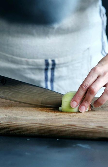 A person is cutting an onion on a wooden cutting board.