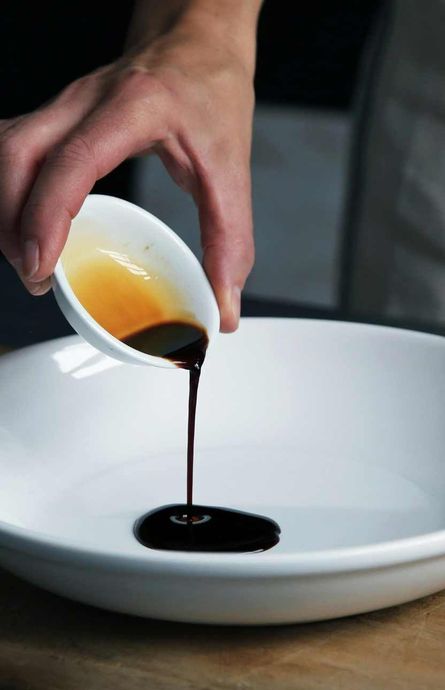 A person is pouring sauce into a white plate.